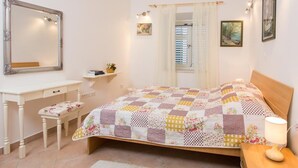 Une chambre à coucher avec un lit, une table de chevet avec une lampe, un bureau avec une chaise, un miroir et une fenêtre avec des rideaux.