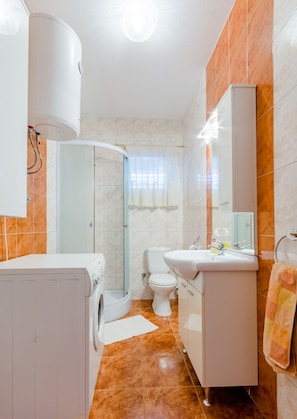 A compact bathroom with a washing machine, toilet, and sink. - Apartments Jerko (Supetar)
