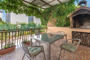 An outdoor patio with a glass table and metal chairs, surrounded by potted plants and a brick wall. - Apartments Jerko (Supetar)