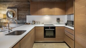 A modern kitchen with wooden cabinets, stainless steel appliances, and a white countertop. - Modern duplex near slopes with parking (Méribel)