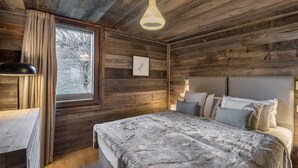 A cozy log cabin bedroom with a bed, bedside lamp, and a window with curtains. - Modern duplex near slopes with parking (Méribel)