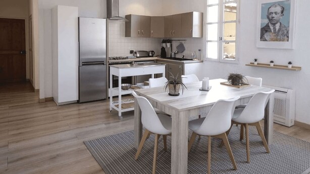 Una cocina moderna con armarios blancos, un refrigerador de acero inoxidable y un comedor con mesa y sillas blancas.
