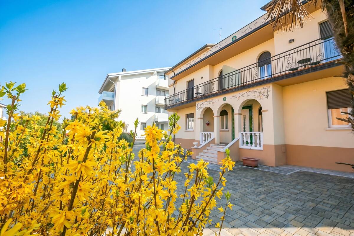 Ein Gebäude mit mehreren Balkonen, einem gepflasterten Innenhof und einem blumenbehangenen Eingang.