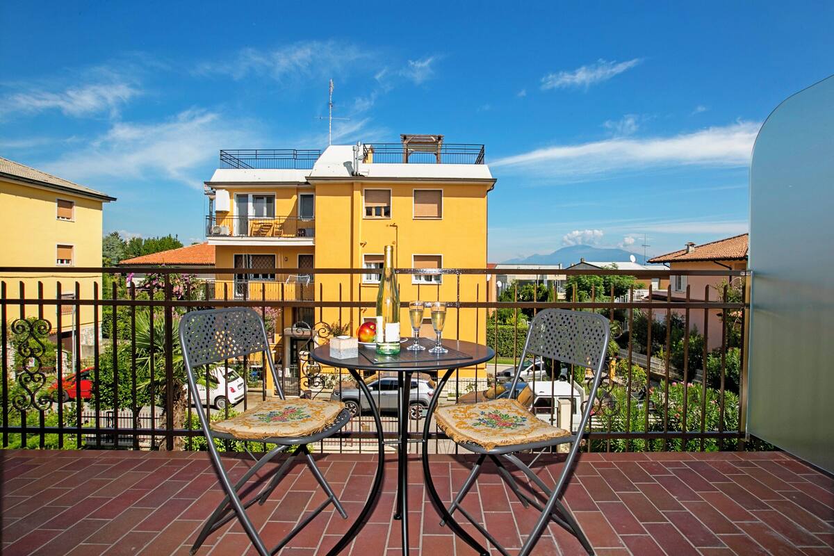 Ein Balkon mit zwei Stühlen, einem Tisch, einer Flasche und Gläsern.