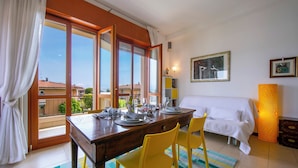 A room with a dining table set for four, a bed, and a large window with curtains. - Casa Michelangelo Lake Garda Terrace Apt Sleeps 6 + AC (Desenzano del Garda)
