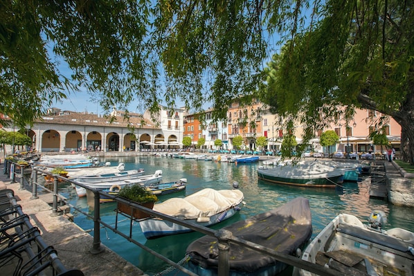 A canal with boats docked, a bridge, and buildings with arches in the background.