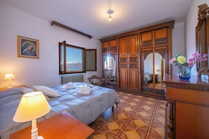 Une chambre d’hôtel avec un lit, une table de chevet, une lampe, une commode, un miroir et une vue sur la mer.