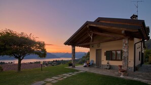 Una casa con fachada de piedra, un porche de madera y vistas a montañas y un lago.
