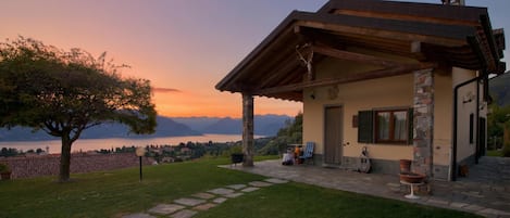 A house with a stone facade, a wooden porch, and a view of mountains and a lake.