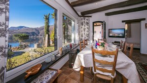 A dining area with a view of a lake and mountains, wooden furniture, and a television in the background. - Morcote Magic View (Morcote)