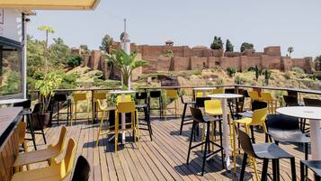 An outdoor patio with yellow and black chairs and tables, overlooking a historic brick wall and greenery.