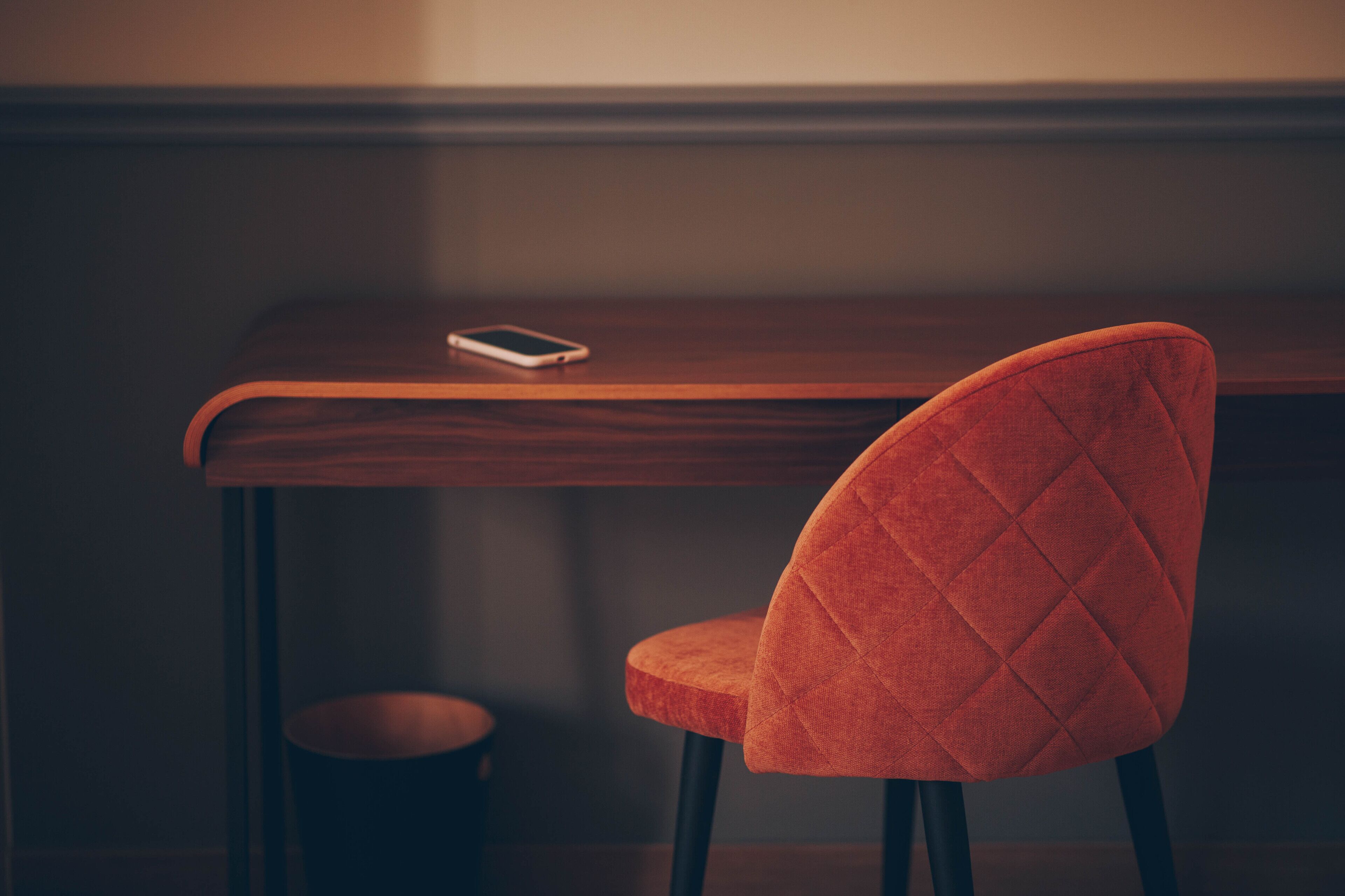 A wooden table with a smartphone on it, a red upholstered chair, and a small round stool.