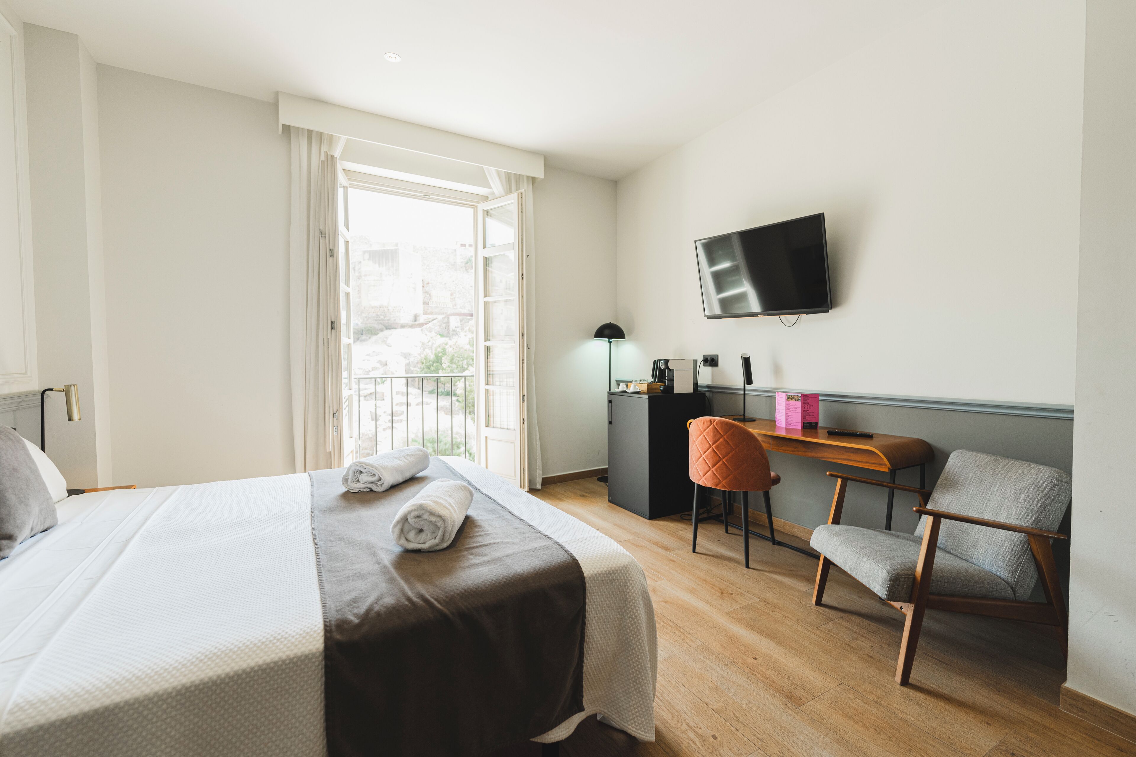 Ein Hotelzimmer mit einem Bett, einem Schreibtisch, einem Stuhl, einem Fernseher und einem Fenster.