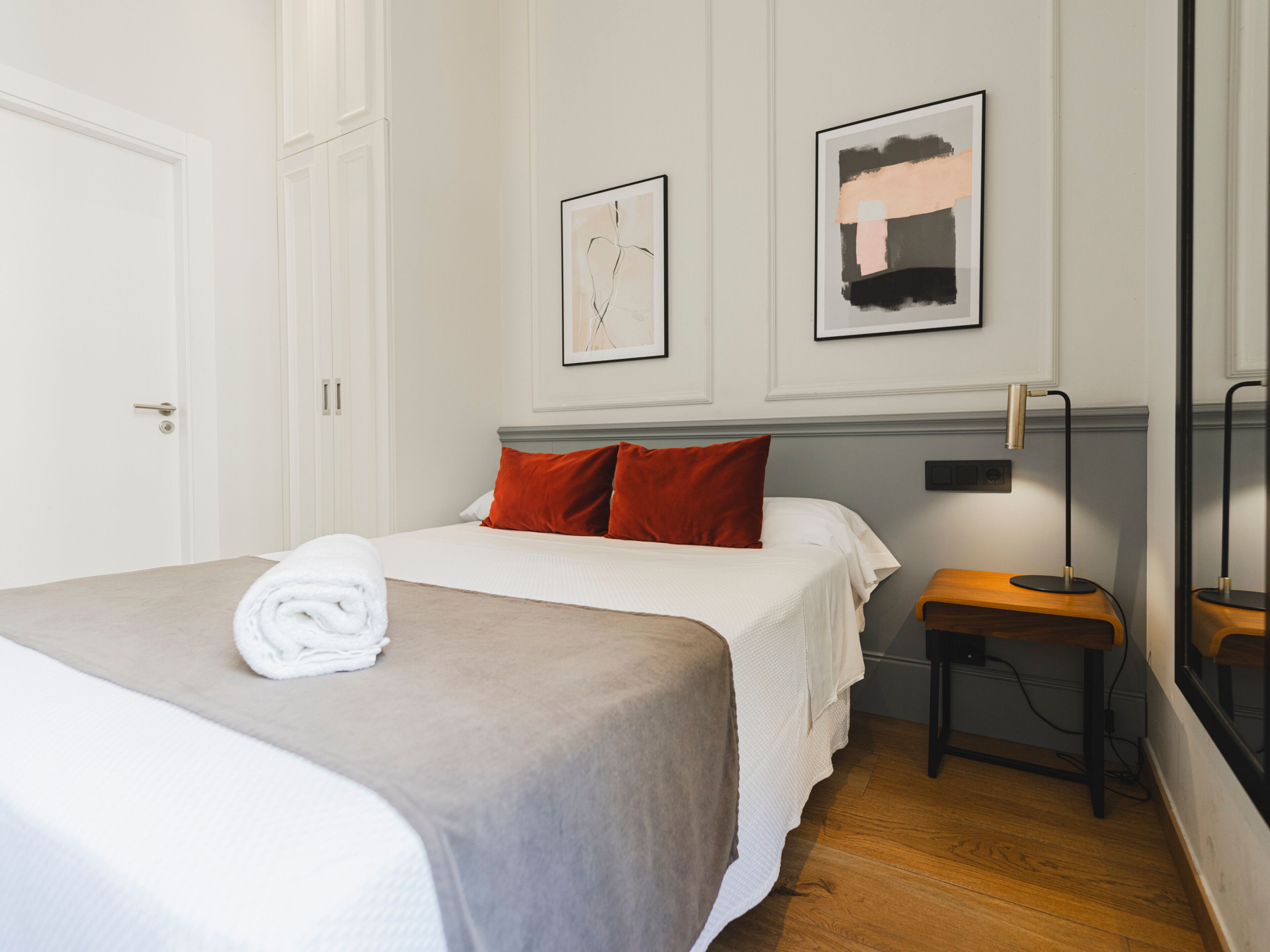 Habitación de hotel ordenada con una cama, una mesita de noche, una silla y dos cuadros en la pared.