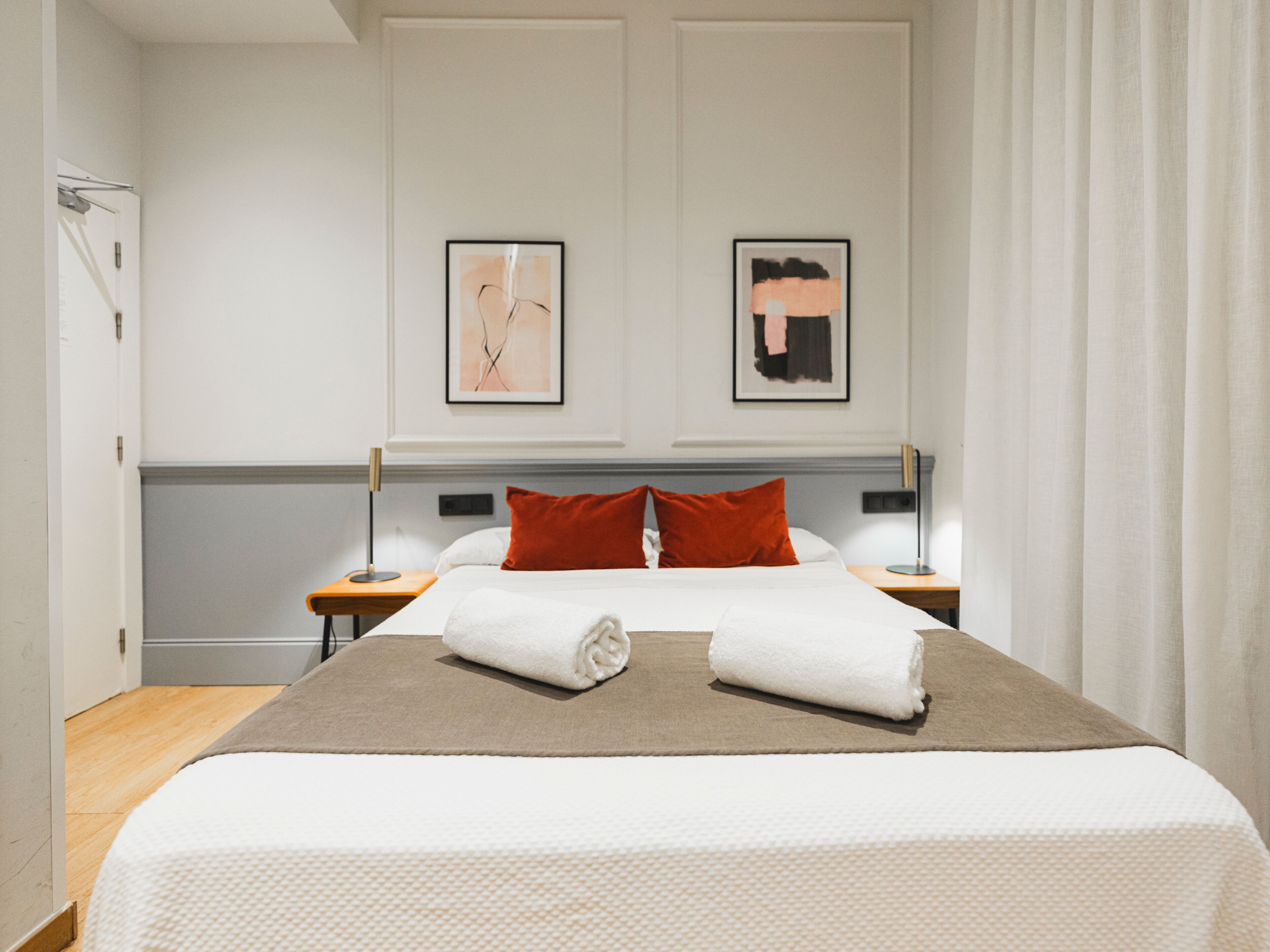 Habitación de hotel con una cama grande, dos mesitas de noche, piso de madera y dos cuadros enmarcados en la pared.