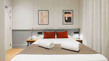 Habitación de hotel con una cama grande, dos mesitas de noche, piso de madera y dos cuadros enmarcados en la pared.
