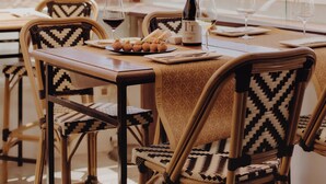 Un espacio de comedor al aire libre con sillas de mimbre y una mesa para dos, con vista a una antigua pared de piedra.