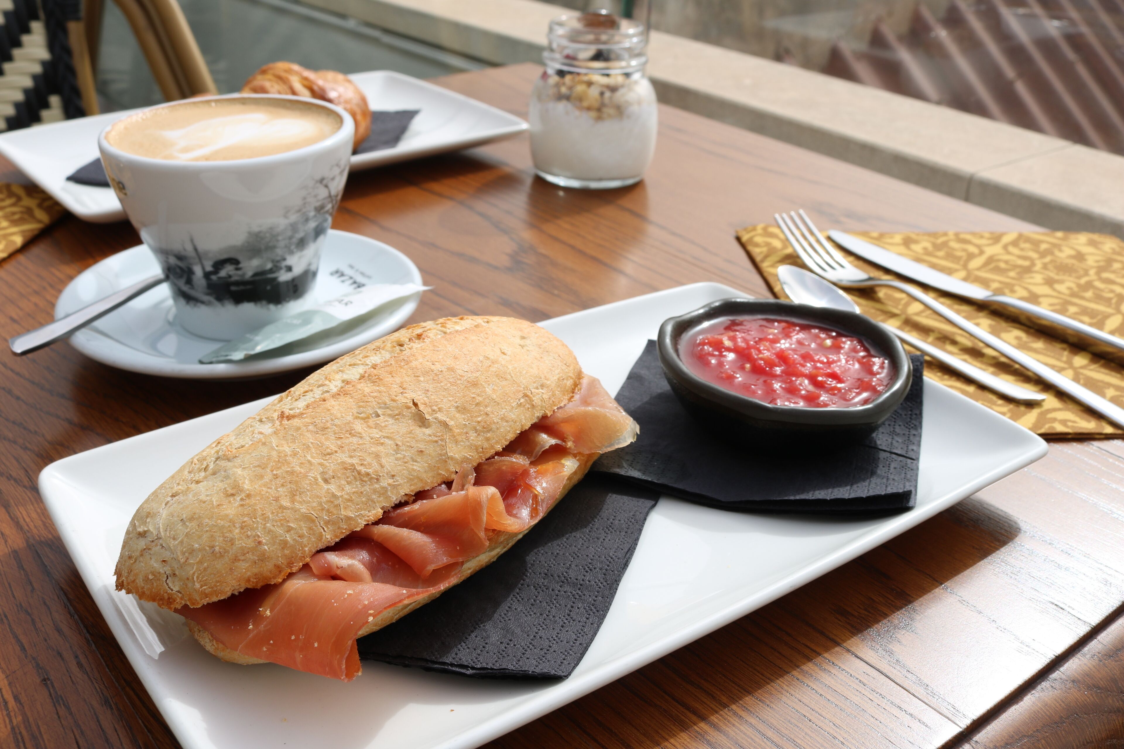 A sandwich with ham and a bowl of red sauce on a white plate.