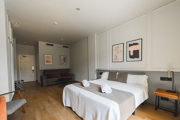 A hotel room with a large bed, a bedside table, a chair, a sofa, and a wall with framed artwork. - Alcazaba Premium Hotel (Málaga)
