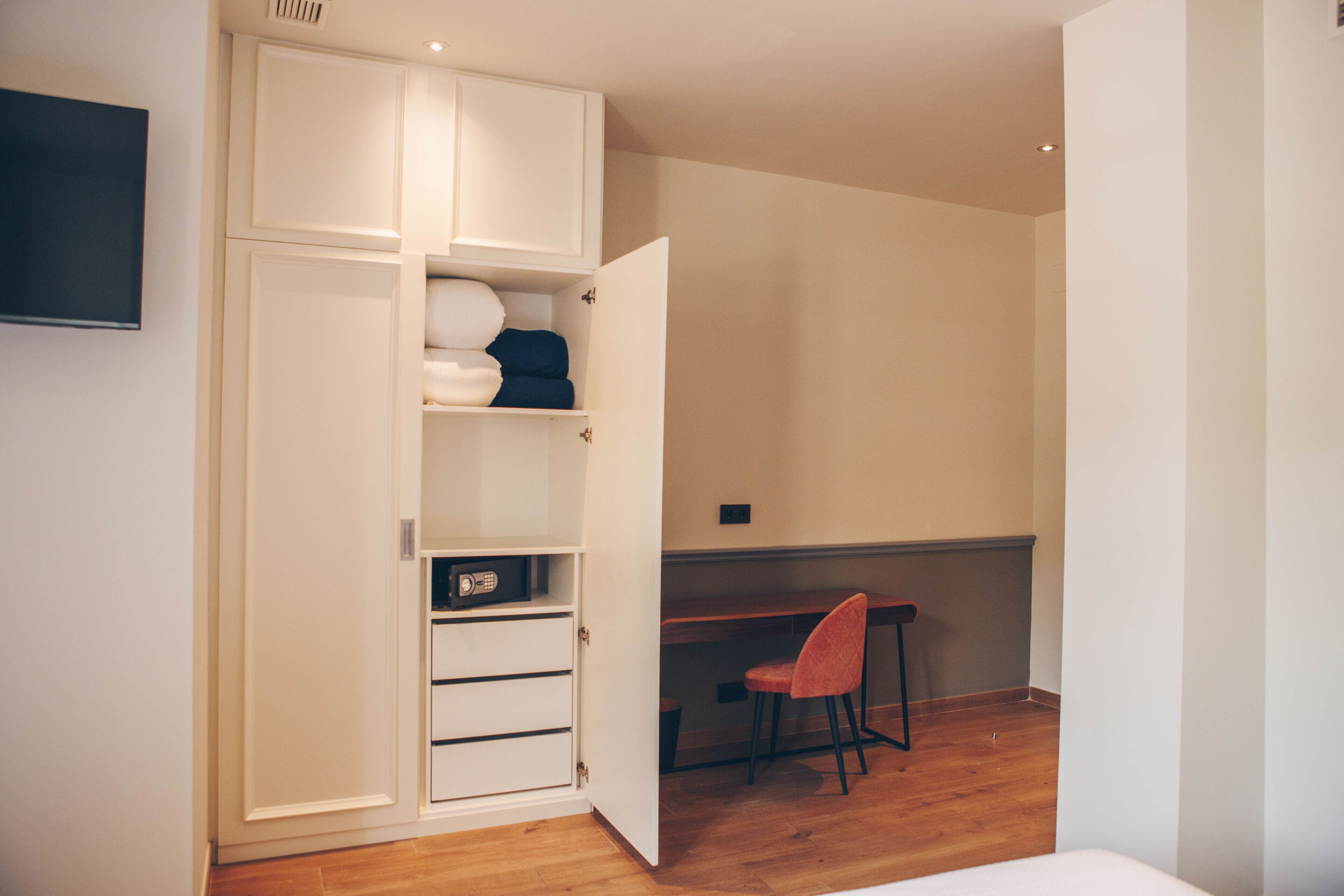 Un dormitorio con cama, escritorio y silla. Se observa un armario con varios compartimentos.