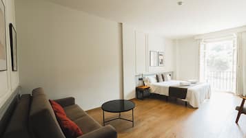 A spacious room with a large bed, a sofa, a small table, and a window with curtains.