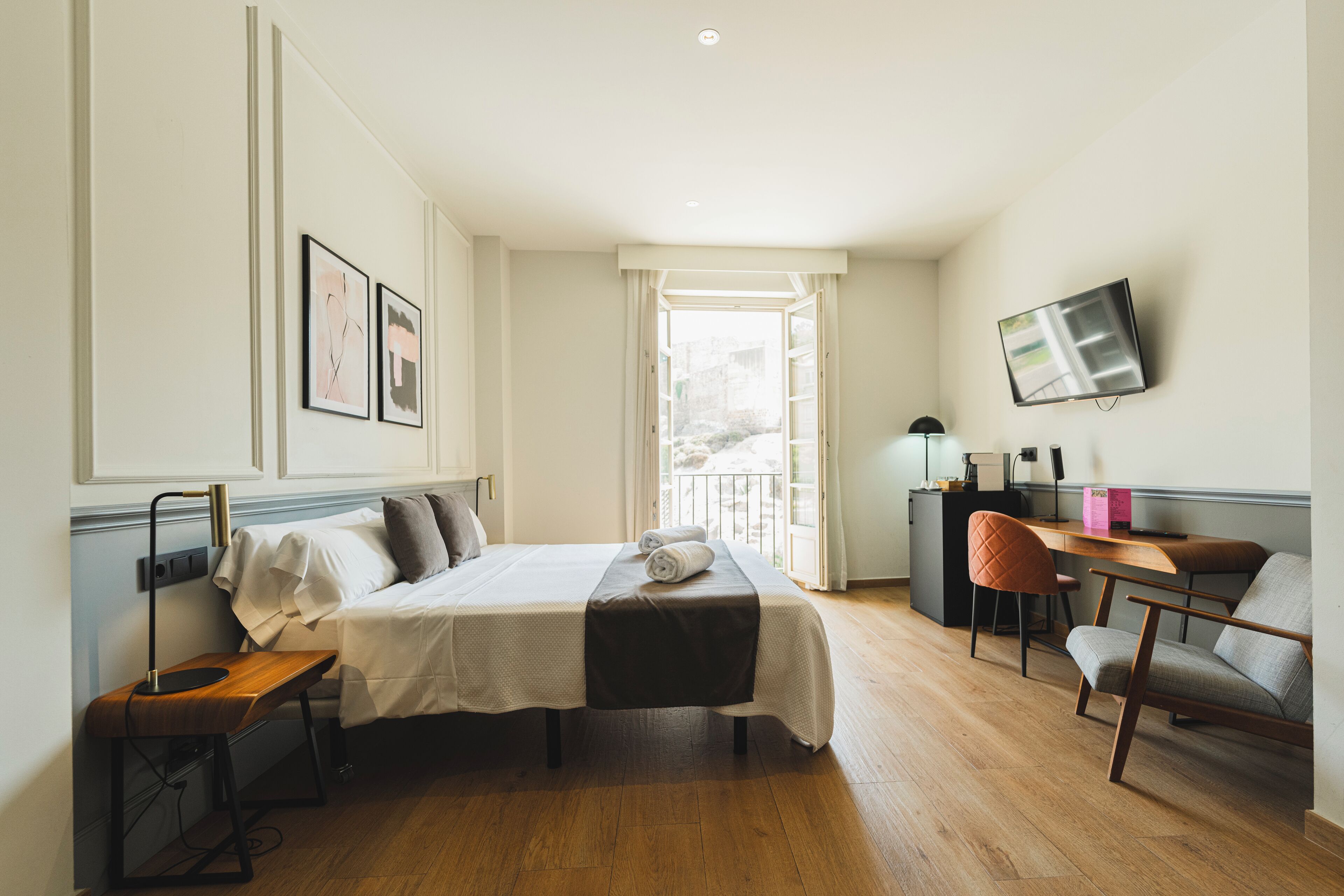 A hotel room with a bed, desk, chair, and a TV mounted on the wall.