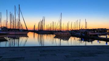 Un port de plaisance au coucher du soleil, avec de nombreux bateaux amarrés, des eaux calmes reflétant les bateaux et un ciel dégagé.