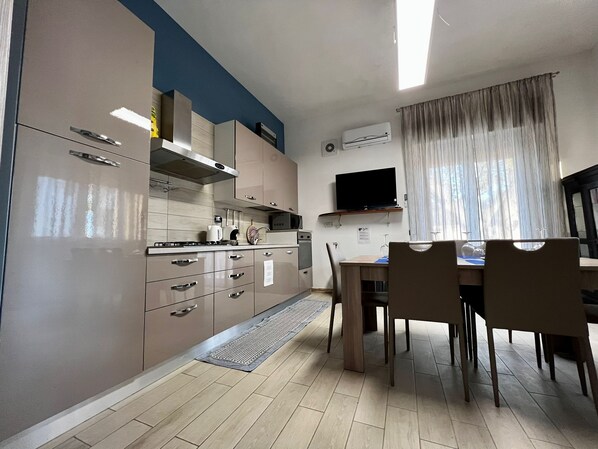 Una cocina compacta con electrodomésticos modernos, una zona de comedor con sillas y un televisor en la pared.