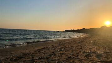 Une plage, un ciel dégagé et le soleil qui se couche à l’horizon.