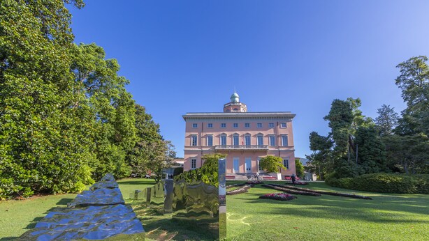Un grand bâtiment doté d’un dôme central et de fenêtres disposées de manière symétrique, entouré de pelouses et d’arbres bien entretenus.