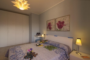 Een slaapkamer met een bed, nachtkastje, bureau, lamp en twee aan de muur bevestigde schilderijen.