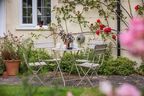 Relax in the serene outdoor seating area with a round table and four chairs, surrounded by lush greenery and vibrant flowers.