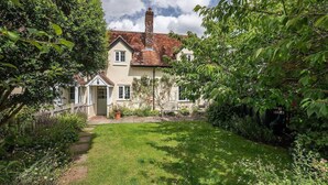 A traditional two-story house with a well-maintained garden, a pathway leading to the entrance, and a visible chimney.