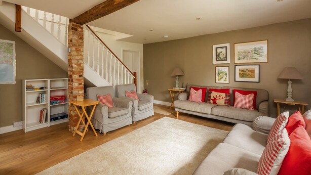 A cozy living room with a staircase, a sofa set, a bookshelf, and framed pictures on the wall.