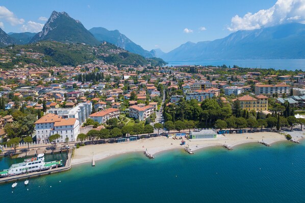 A coastal town with a marina, buildings with red roofs, and a mountainous backdrop.