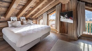 A bedroom with a large bed, wooden beams, a TV, and a view of a snowy landscape. - Modern family chalet near slopes with parking (Méribel)