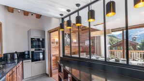 A modern kitchen with a built-in oven, a coffee maker, and a dining area with a view of the mountains. - Modern family chalet near slopes with parking (Méribel)