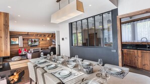A modern dining area with a long table set for a meal, a cozy seating area with a fireplace, and a large window offering a view of the outdoors. - Modern family chalet near slopes with parking (Méribel)