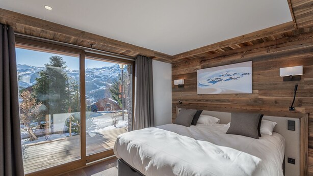 A bedroom with a large bed, wooden ceiling, a view of mountains, and a painting on the wall. - Modern family chalet near slopes with parking (Méribel)
