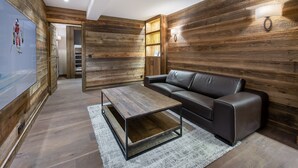 A modern living room with a wooden wall panel, a black leather sofa, a wooden coffee table, and a white rug. - Modern family chalet near slopes with parking (Méribel)