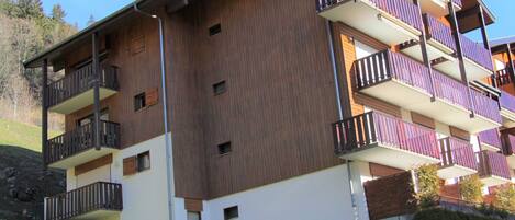 A multi-story building with balconies, a flat roof, and a grassy area in front.