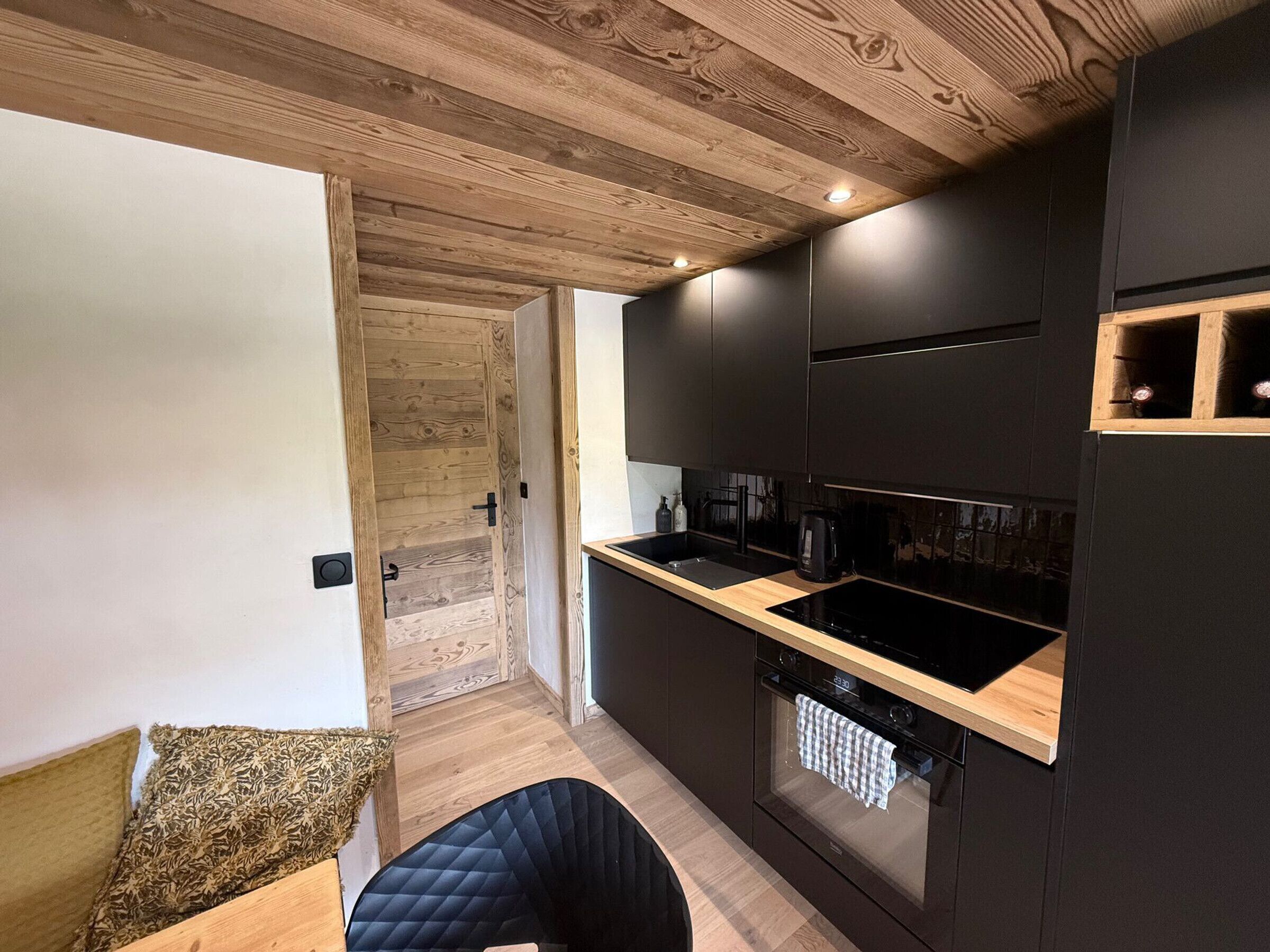 Una cocina moderna con armarios oscuros, techo de madera y horno empotrado.
