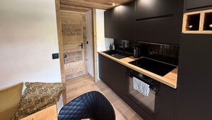 Una cocina moderna con armarios oscuros, techo de madera y horno empotrado.