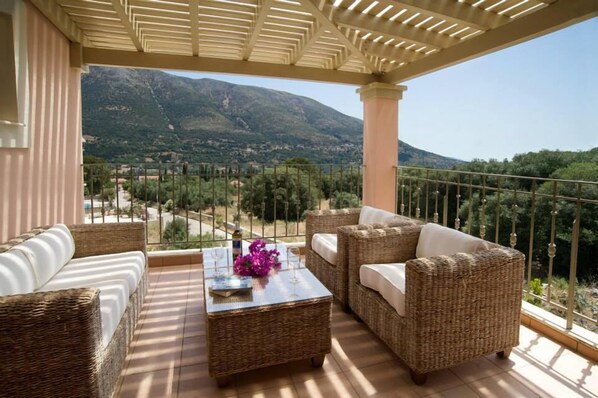 A balcony with wicker furniture, a glass table, and a view of mountains.