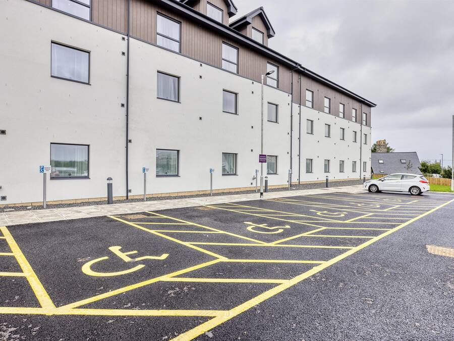 A parking area with disabled parking spaces, a building with multiple windows, and a car parked in the distance.