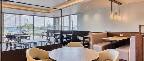 A modern restaurant with round tables, cushioned booths, and large windows offering a view of the parking lot.