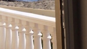 Ein Balkon mit weißen Brüstungen, der auf eine felsige Küste und ein Gewässer blickt.