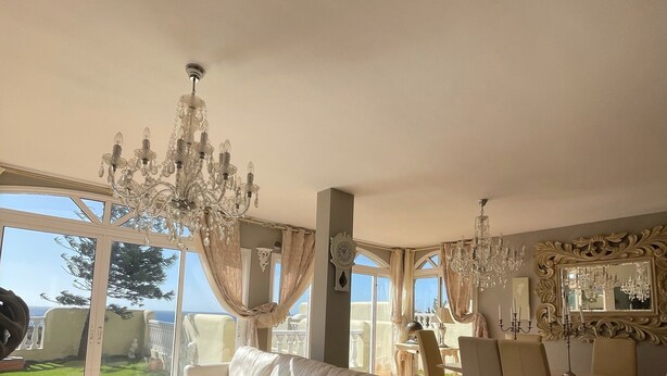 Ein großzügiges Wohnzimmer mit einem großen weißen Sofa, einem Essbereich mit Tisch und Stühlen sowie einer Deckenleuchte.