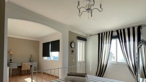 Ein Schlafzimmer mit einem großen Bett, einem Schreibtisch und einem Sessel, einer Kristallleuchter und einem Fenster mit Vorhängen.
