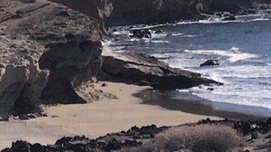 Ein felsiger Strand mit brechenden Wellen und einer steilen Klippe im Hintergrund.